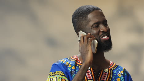 Close-up-view-of-young-cheerful-African-American-man-in-traditional-clothes-talking-on-the-phone
