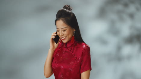 Asiatische-Junge-Fröhliche-Frau-In-Roter-Traditioneller-Kleidung,-Die-Fröhlich-Am-Handy-Spricht