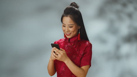 Asiatische-Junge,-Fröhliche-Frau-In-Roter-Traditioneller-Kleidung,-Die-Fröhlich-Auf-Dem-Handy-Eine-Sms-Schreibt