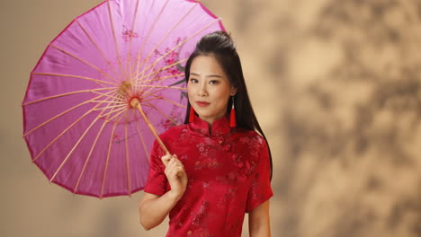 Porträtaufnahme-Einer-Jungen,-Fröhlichen-Asiatin-In-Roter-Traditioneller-Kleidung,-Die-Einen-Sonnenschirm-Hält,-Während-Sie-In-Die-Kamera-Lächelt