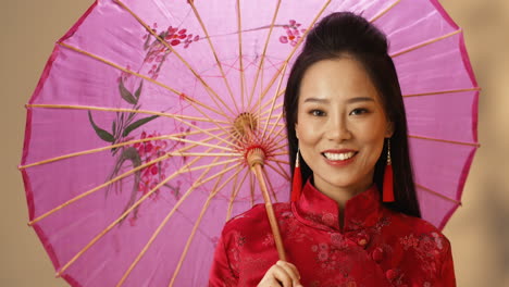 Nahaufnahme-Einer-Asiatischen-Jungen,-Fröhlichen-Frau-In-Roter-Traditioneller-Kleidung,-Die-Einen-Sonnenschirm-Hält,-Während-Sie-In-Die-Kamera-Lächelt