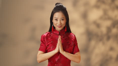 Porträt-Einer-Jungen-Asiatischen-Frau-In-Roter-Traditioneller-Kleidung,-Die-Fröhlich-In-Die-Kamera-Lächelt-Und-Eine-Grußgeste-Macht