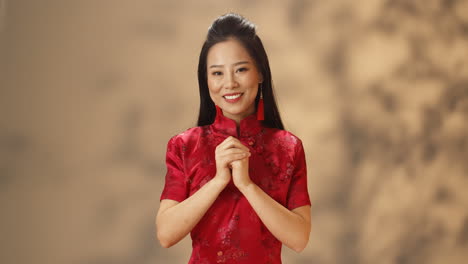 Porträt-Einer-Jungen-Asiatischen-Frau-In-Roter-Traditioneller-Kleidung,-Die-Fröhlich-In-Die-Kamera-Lächelt-Und-Mit-Den-Händen-Eine-Chinesische-Glückwunschgeste-Macht