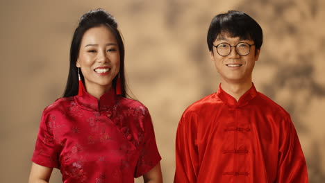 Fröhliches-Junges-Asiatisches-Paar-In-Roter-Traditioneller-Kleidung,-Das-Sich-Ansieht-Und-Fröhlich-In-Die-Kamera-Lächelt