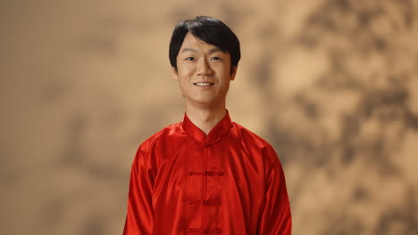 Fröhlicher-Junger-Asiatischer-Mann-In-Roter-Traditioneller-Tracht,-Der-In-Die-Kamera-Lächelt