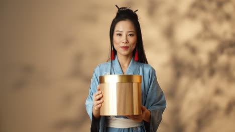 Junge-Asiatische-Frau-Im-Blauen-Kimono,-Der-Eine-Goldene-Schachtel-Hält-Und-Sie-Der-Kamera-Zeigt