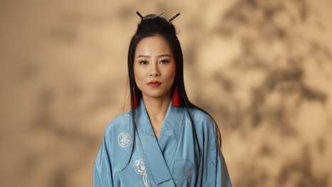 Junge-Asiatische-Frau-Im-Blauen-Kimono,-Die-Mit-Ernstem-Ausdruck-Zur-Kamera-Schaut