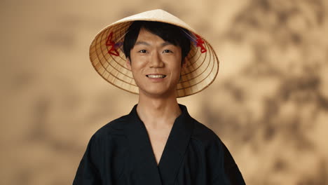 Junger-Asiatischer-Mann-In-Schwarzer-Traditioneller-Tracht-Und-Konushut,-Der-In-Die-Kamera-Lächelt