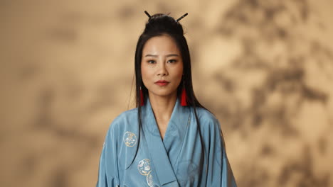Porträtaufnahme-Einer-Jungen-Asiatischen-Wütenden-Frau-Im-Blauen-Kimono,-Die-Mit-Ernster-Miene-In-Die-Kamera-Schaut-Und-Mit-Der-Faust-Schlägt