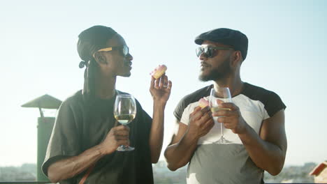 Gay-couple-standing-on-rooftop-with-glasses-of-wine-and-donuts