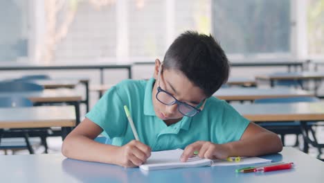 Niño-Alumno-Latino-Enfocado-Con-Gafas-Escribiendo-En-Papel