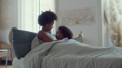 Relaxed-African-American-mum-and-her-little-daughter-lying-in-bed-on-lazy-weekend