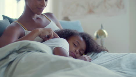 Close-up-of-little-Black-girl-lying-on-her-mum's-knees-in-bed,-then-opening-her-eyes-and-smiling