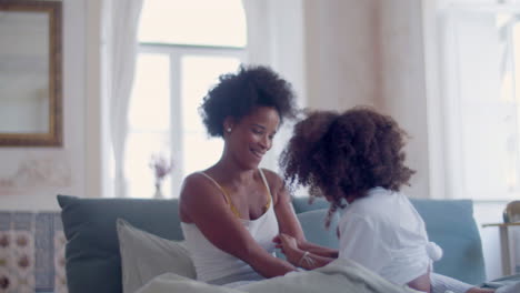 Cheerful-African-American-mum-and-daughter-tickling-each-other-in-bed,-laughing-and-having-fun-together