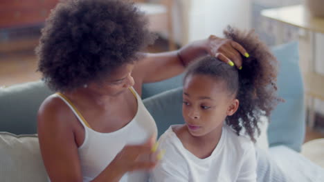 African-American-woman-combing-daughter's-hair-and-doing-a-ponytail