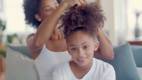 African-American-mother-combing-daughter's-hair-while-little-girl-smiling-and-looking-at-the-camera