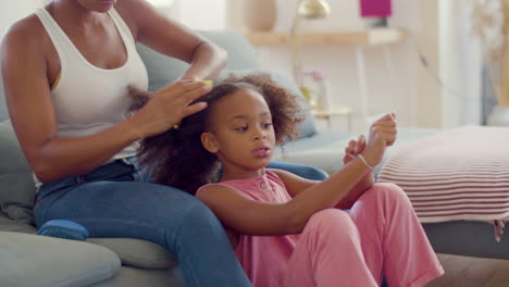 African-American-mum-tying-up-her-little-daughter's-into-pigtails-at-home