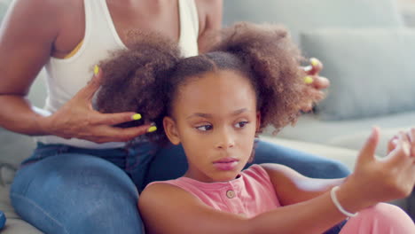 Black-woman-sitting-on-couch-touching-her-daughters-pigtails