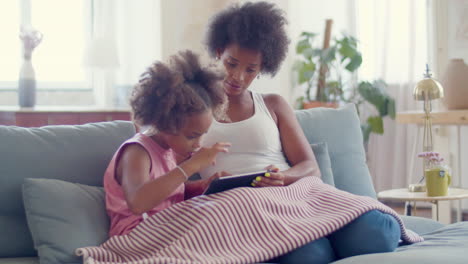 Mujer-Negra-Concentrada-Ayudando-A-Una-Linda-Hija-A-Estudiar-En-Línea-En-Una-Tableta-Digital