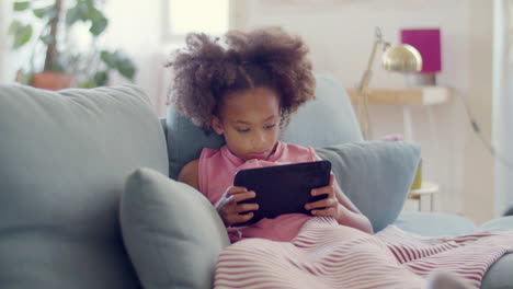 Cute-Black-girl-enjoying-mobile-game-on-tablet-lying-in-bed