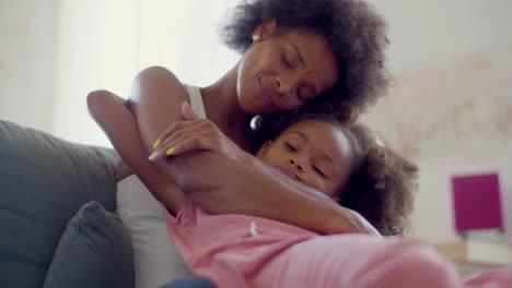 Loving-Black-woman-and-cute-little-girl-sitting-on-couch-and-hugging-at-home