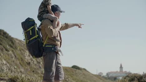 Tracking-shot-of-father-carrying-his-son-on-shoulders-while-hiking-in-mountains