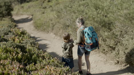Woman-with-backpack-holding-child's-hand-walking-down-dirt-road