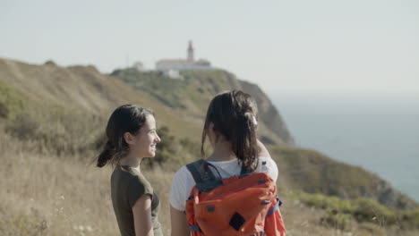 Two-girls-standing-on-mountain-cliff,-enjoying-stunning-sea-view