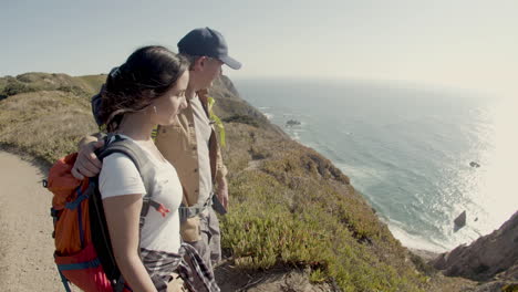 Father-and-daughter-hiking-at-mountain-top,-standing-on-cliff-and-enjoying-view-of-sea