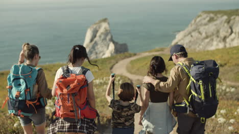 Back-view-of-a-Caucasian-family-with-backpacks-walking-down-dirt-road-towards-the-sea