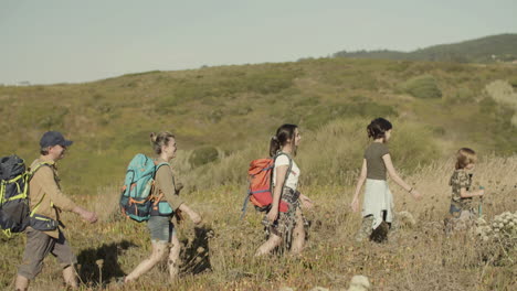 Side-view-of-happy-family-with-backpacks-walking-along-hiking-trail-in-row