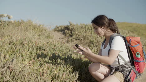 Pretty-Caucasian-girl-with-backpack-taking-photo-of-flowers-with-phone