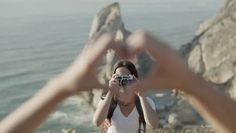 Girl-taking-photo-of-two-unrecognizable-people-doing-heart-gesture-during-hiking-adventure
