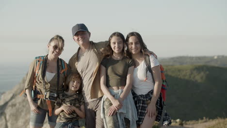 Front-view-of-a-happy-family-standing-on-cliff-and-smiling-at-the-camera