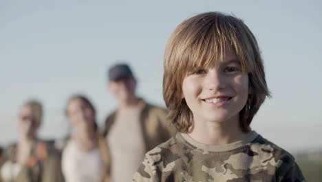 Portrait-of-a-little-Caucasian-boy-looking-at-the-camera-and-smiling-while-his-family-standing-behind-in-a-blurred-background