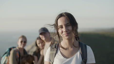 Smling-hiker-girl-looking-at-the-camera-while-her-family-standing-behind-in-a-blurred-background