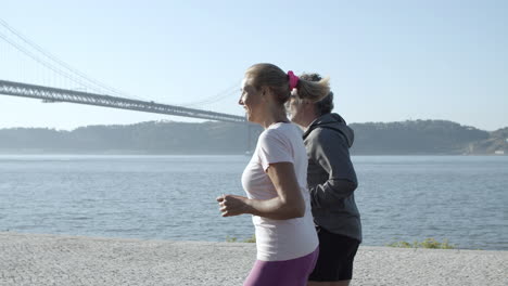 Caucasian-couple-jogging-along-sea,-talking-and-smiling