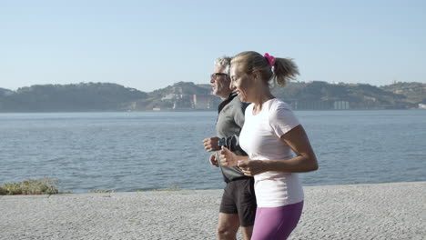 Active-couple-training,-jogging-along-sea-and-smiling