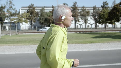 Side-view-of-active-male-pensioner-with-hearing-aid-device-jogging-outside