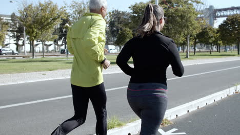 Couple-of-mature-runners-jogging-down-street