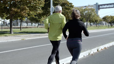 Couple-of-older-60s-runners-jogging-down-street