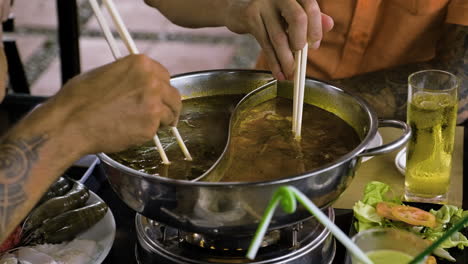 Friends-putting-meat-inside-hot-pot-in-the-restaurant