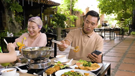 Chinesische-Familie,-Die-Leckeres-Essen-Isst,-Während-Einer-Von-Ihnen-Sich-Auf-Sein-Smartphone-Konzentriert