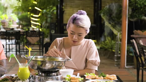 Young-asian-woman-eating-food-from-hot-pot
