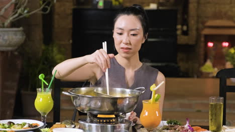 Young-brunette-woman-putting-some-meat-inside-hot-pot-with-chopsticks