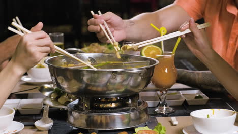 People-taking-delicious-ingredients-from-hot-pot-in-middle-of-the-table