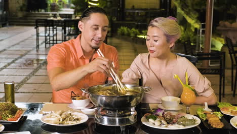 Cheerful-woman-and-man-taking-mushrooms-with-chopsticks-from-hot-pot