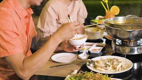 Young-man-eating-noodles-and-woman-eating-vegetables-from-bowl