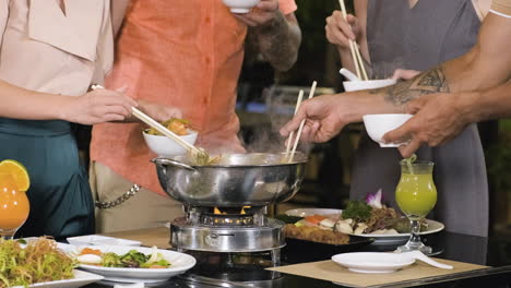 People-standing-and-picking-food-from-hot-pot-to-their-white-bowls