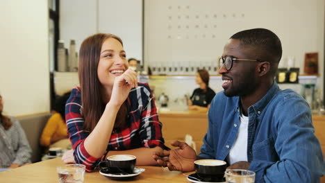 Caucasian-woman-and-african-american-man-talking-sitting-at-a-table-in-a-cafe